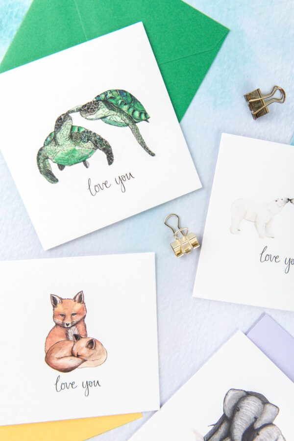Selection of cards with pairs of animals illustrated and 'love you' hand lettered text printed beneath each couple.