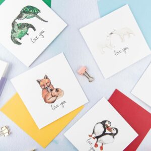 Selection of cards with pairs of animals illustrated and 'love you' hand lettered text printed beneath each couple.