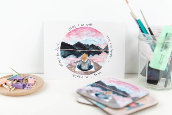 Postcard with illustration of meditating girl sat beneath mountains, with hand lettered words 'May I be well... may I be happy... may I be peaceful... may I be loved'.