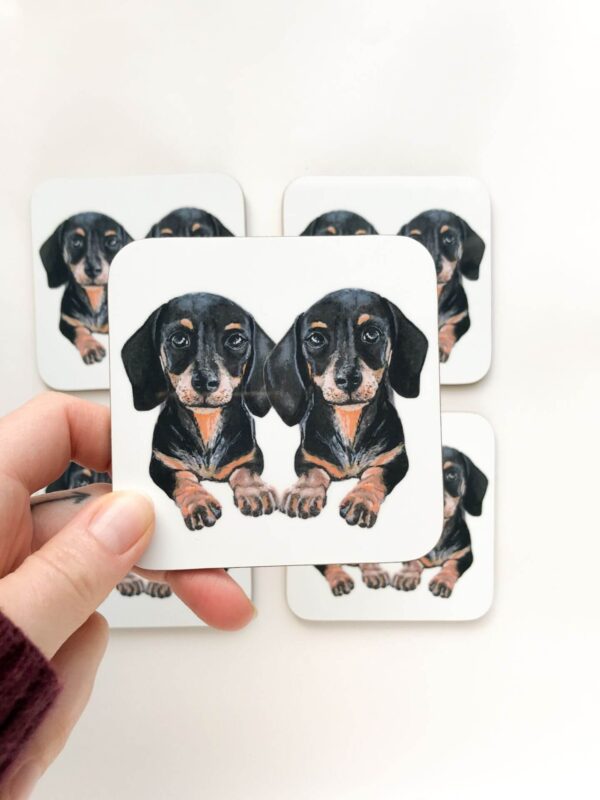 Stack of coasters with illustrated design of 2 cute black and tan sausage dogs
