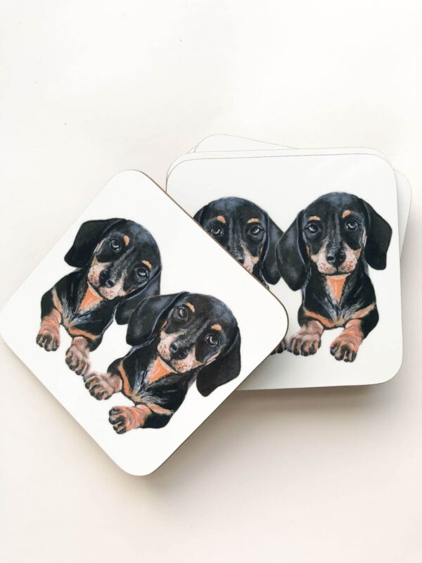 Stack of coasters with illustrated design of 2 cute black and tan sausage dogs
