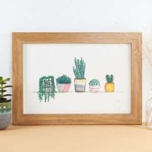 Framed print with cute little house plants and succulents on a shelf.