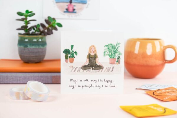 Illustrated card of a girl calmly meditating surrounded by house plants, with hand lettered quote reading 'may I be well, may I be happy, may I be peaceful, may I be loved'.