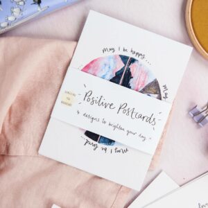 Pack of positive postcards by Sunshine for Breakfast, scattered on a table with a soft linen scarf and BeeFayre handcream
