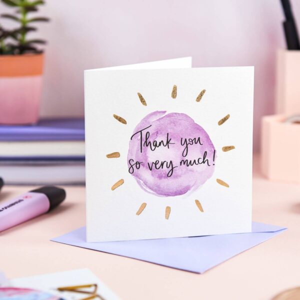 Pretty desk featuring 'thank you so much' card with simple purple design and gold foil detail