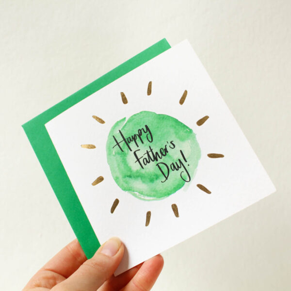 A hand holding a Father's Day card in simple green and gold design.