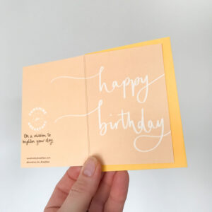 happy birthday notecard, held displaying the detail of hand lettered text that flows from the front to back of the card