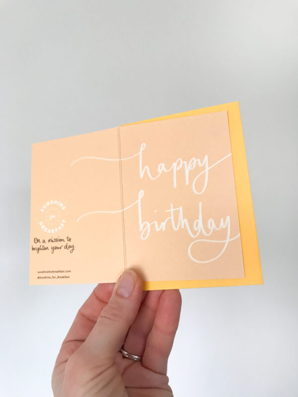 happy birthday notecard, held displaying the detail of hand lettered text that flows from the front to back of the card