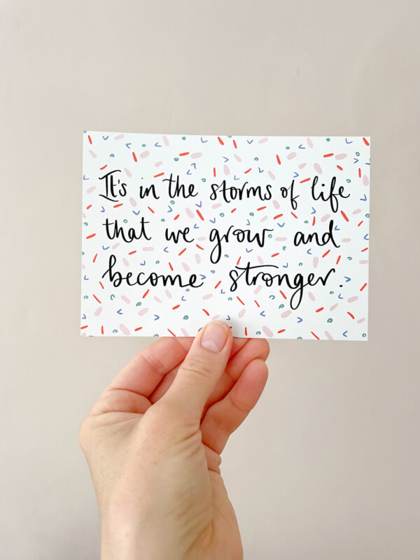 Hand holding a postcard, reading 'It's in the storms of life that we grow and become stronger'.