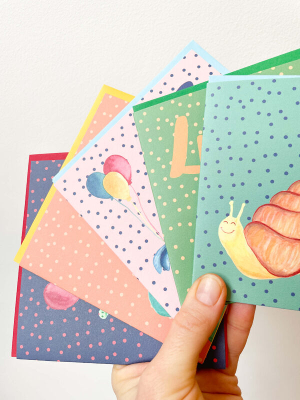 Hand holding colourful children's birthday cards featuring animals and balloons