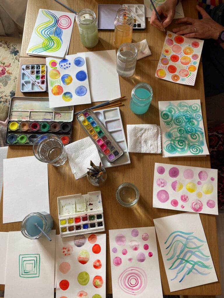 Watercolour workshops - workshop table with paints, water and colourful painted patterns