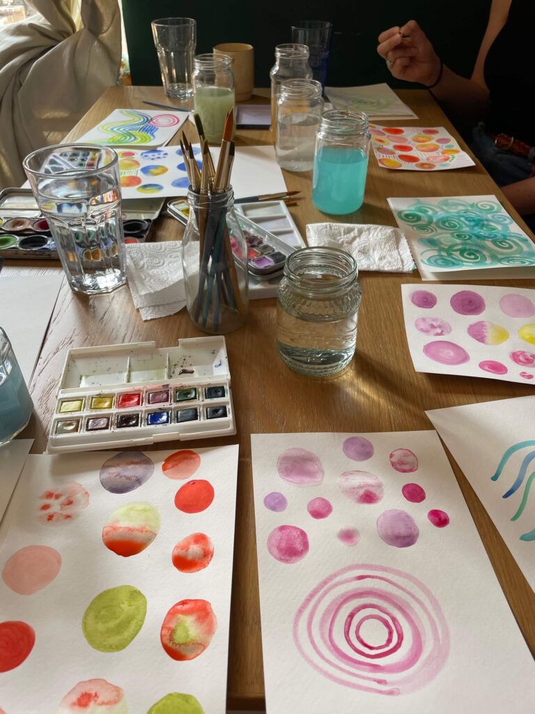 Watercolour workshops - workshop table with paints, water and colourful painted patterns